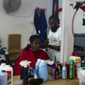 Una mujer haitiana recibe un corte de cabello en una barbería instalada por un ciudadano haitiano en Tapachula. Foto de Javier García