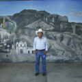 Don Teo. Detrás hay un mural ubicado en el centro del municipio. A su izquierda, la ilustración de la iglesia de San Francisco y la llegada del primer automóvil al municipio. Foto: Salvador Vázquez.