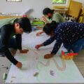 Alejandro Valdez, izquierda, Margarita Velasco, derecha, y Luis Cárdenas, detrás de Velasco, estudiantes de la maestría en recreación comunal en la Universidad Autónoma Comunal de Oaxaca, pintan durante una clase en San Pablo Etla. Ena Aguilar Peláez, Global Press Journal Mexico.
