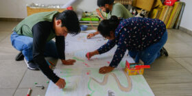 Alejandro Valdez, izquierda, Margarita Velasco, derecha, y Luis Cárdenas, detrás de Velasco, estudiantes de la maestría en recreación comunal en la Universidad Autónoma Comunal de Oaxaca, pintan durante una clase en San Pablo Etla. Ena Aguilar Peláez, Global Press Journal Mexico.
