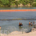 Migrantes caminan junto a una cadena de boyas colocadas en el agua a lo largo de la frontera del Río Grande con México en Eagle Pass, Texas, el 16 de julio de 2023. El gobierno mexicano informó el 2 de agosto de 2023 que se había encontrado un cadáver atrapado en las polémicas barreras flotantes instaladas por las autoridades de Texas para detener el cruce de migrantes hacia Estados Unidos. Foto: Suzanne Cordeiro / Archivo AFP